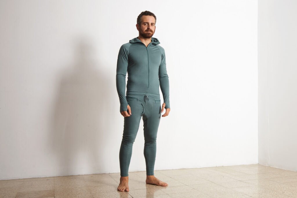 young athlete wers green merino wool baselayer thermal suite winter time posing front white wall 2